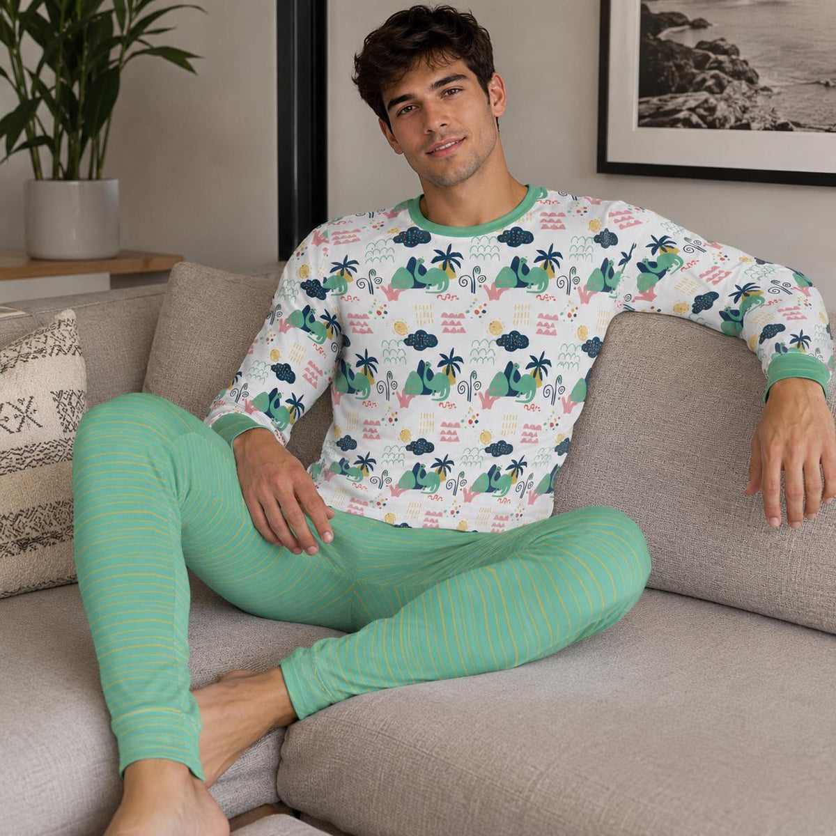 Man wearing two-piece ABDL pajama set featuring a cute dinosaur and palm print top with sage green striped pants
